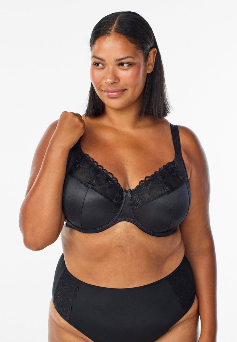 Black bra with lace detailing and scalloped edges; padded cups, adjustable straps, and a decorative bow at the center. Paired with high-waisted black briefs.