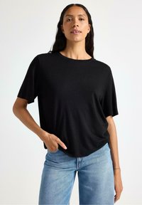 Zwarte korte mouwen t-shirt in een zachte, gladde stof met een ronde hals, gecombineerd met lichtblauwe hoge taille jeans. Casual pasvorm.
