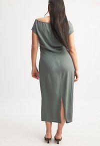 Olive green dress with a textured fabric, short sleeves, a back slit, and a fitted silhouette, paired with black high-heeled sandals.