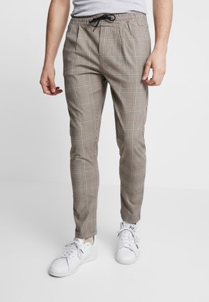 Pantalons à carreaux marron avec une taille élastique, présentant une coupe slim et une texture lisse, associés à des baskets blanches.
