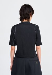 Black, short-sleeve top with a textured fabric and contrasting grey stitching. Features a round neckline and a cropped fit.