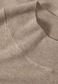 Beżowy sweter dzianinowy o prążkowanej fakturze i zaokrąglonym, plisowanym kołnierzu. Materiał wydaje się miękki i lekki.