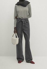 Gestreifter Langarmoberteil in Schwarz und Weiß, kombiniert mit hoch taillierten, weit geschnittenen dunkelblauen Jeans. Eine weiße Handtasche und rote Schuhe runden den Look ab.