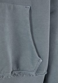 Gray sweatshirt featuring a kangaroo pocket, textured fabric, raw-edge hem, and ribbed cuffs for added detail and texture.