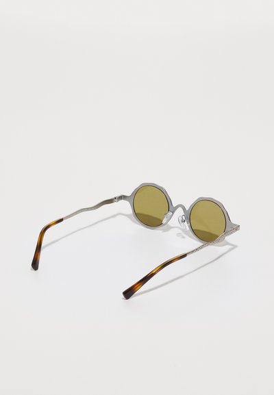 Ochelari de soare rotunzi cu rame metalice argintii și lentile cu nuanță verde. Accente texturate pe margini; brațele au un design bicolor cu motive de țestoasă.