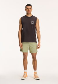 Sort ærmeløs skjorte med brystlomme og grafisk detalje, parret med lysegrønne shorts og orange høj-top sneakers.