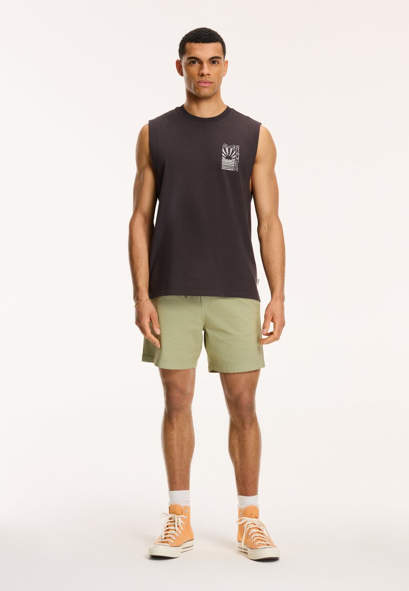 Sort ærmeløs skjorte med brystlomme og grafisk detalje, parret med lysegrønne shorts og orange høj-top sneakers.