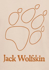 Καφέ περίγραμμα αποτυπώματος πατούσας λύκου πάνω από το κείμενο «Jack Wolfskin» σε μπεζ φόντο.