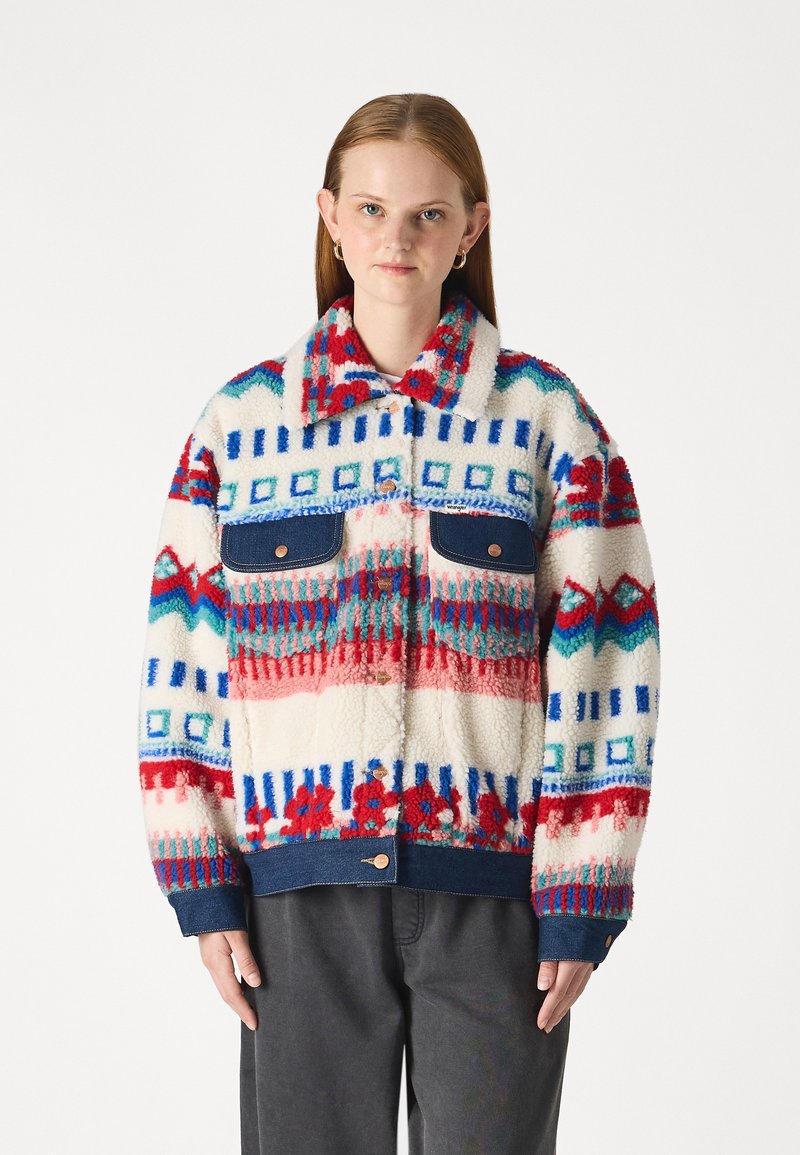 Chaqueta de forro polar con un patrón geométrico multicolor en rojo, azul y crema, con acentos de mezclilla y dos bolsillos frontales.