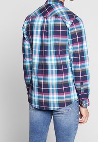 Chemise à carreaux bleue, rose et verte avec des manches longues, des poignets boutonnés et un design de double épaules. Fabriquée en tissu texturé ; pli dans le dos pour un ajustement.