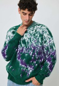 Pull en maille vert et blanc avec une texture duveteuse, présentant un motif dégradé de taches violettes et un col rond.