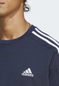 Mornarsko plava pamučna majica s rebrastim okruglim izrezom, bijelim trostrukim dizajnom na ramenima i malim bijelim Adidas logotipom na prsima.