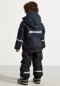 Svart vattentät overall med reflexband, huva och elastiska ärmslut. Den har ett hållbart material och en lös passform för komfort.