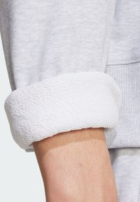 Polsino di felpa grigia in cotone con fodera in spugna bianca. La texture è morbida, con dettagli a coste e una vestibilità ampia.