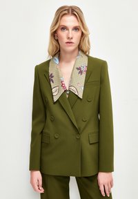 Olivgrön dubbelknäppt kavaj med en blommönstrad beige krage och knappdetaljer. Slät tyg med strukturerad design.