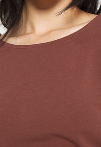 Brązowa, elastyczna bluzka z dekoltem w serek. Gładka tekstura, dopasowany krój i brak widocznych wzorów lub dodatków.