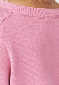 Růžový pletený svetr s žebrovaným výstřihem a čistým šitím, s hladkou texturou a uvolněným střihem, zobrazený zezadu.