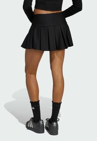 Čierna plisovaná sukňa s vysokým pásom, spárovaná s čiernymi ponožkami s volánikovým okrajom a čiernymi teniskami s bielymi prúžkami.