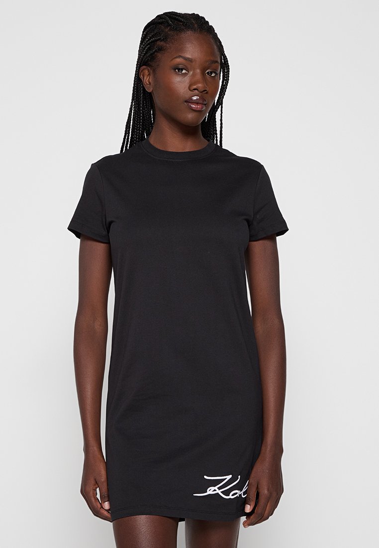 Robe noire à manches courtes en coton. Présente un col rond et un logo brodé blanc sur le bas à gauche. Texture lisse.
