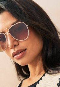 Ochelari de soare aviator supradimensionați cu lentile degradé maro, ramă metalică argintie și design cu dublu pod. Piele netedă și păr închis la culoare accentuează produsul.