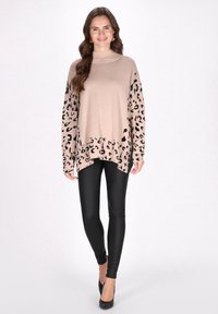 Beige pulóver fekete leopárdmintás ujjakkal és aljjal, garbós, laza szabású, fekete leggingssel és magassarkú cipővel párosítva.