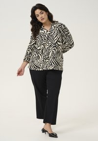 Gemusterte Bluse mit schwarz-weißen Zebra-Streifen, entspannte Passform, kombiniert mit schwarzen, geraden Hosen und glänzenden schwarzen Absatzmulas.