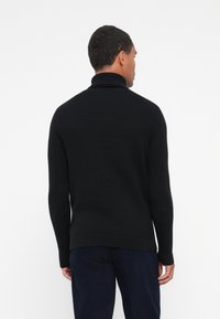 Maglione nero a collo alto lavorato a maglia con polsini e orlo a costine, caratterizzato da un design semplice e texture. Il modello è visto dal retro.