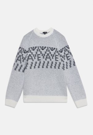 Sweter dziany z długim rękawem, z białymi, czarnymi i szarymi wzorami geometrycznymi na klatce piersiowej i rękawach na jednolitym tle.