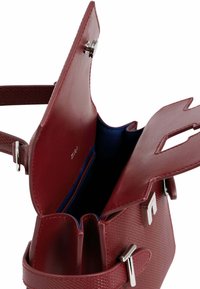 Sac à main en cuir rouge avec un design structuré, dotée d'une doublure intérieure bleue, de quincaillerie en argent et de deux compartiments ouverts.
