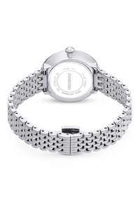 Edelstahl-Uhr mit silbernem Mesh-Armband, rundem Gehäuse und mit Kristallen besetzter Krone. Die Rückseite ist mit "Swarovski" und Angaben zur Wasserbeständigkeit graviert.