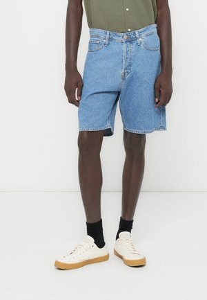Light blue denim shorts with a relaxed fit, a mid-rise waist, and frayed hem. Paired with a dark green shirt and cream sneakers.