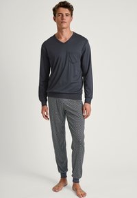 Maglioncino navy a maniche lunghe con scollo a V e taschino sul petto abbinato a pantaloni da pigiama con motivo nelle tonalità di blu e verde, con caviglie arricciate.