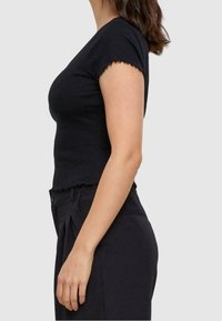 Černý krátký rukáv top vyrobený z vroubkovaného materiálu s volánkovým spodním lemem a rukávy, přiléhavý design zvýrazňující siluetu.