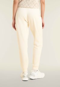 Pantalones joggers color crema con un ajuste relajado, cinturilla elástica y tobillos ajustados, combinados con zapatillas blancas con detalles en plata.