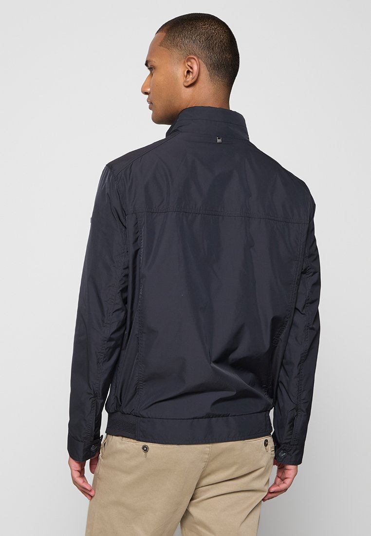 Marineblaues, leichtes Jacket mit Stehkragen, Frontnähten, elastischen Bündchen und tailliertem Saum. Glattes, wasserabweisendes Material.