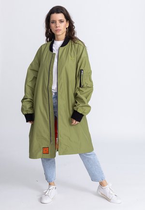 Olijfgroene bomberjack met een rits, geribbelde zwarte manchetten en een utility zak. Gevoerd met rood, met een oranje label aan de zoom.