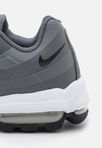 Tenisky Nike Air Max s šedou síťovinou, texturovanými detaily, černým logem swoosh, bílou mezipodešví a viditelným prvkem vzduchového odpružení.