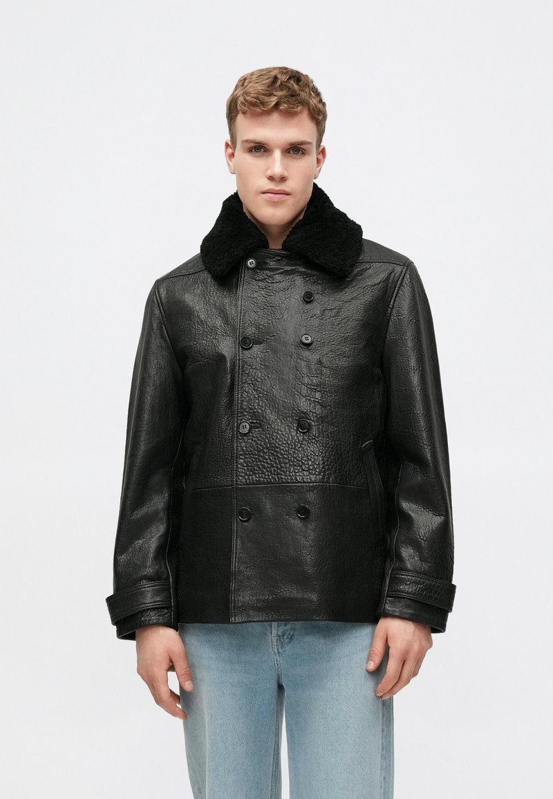 Veste noire en cuir double boutonnage avec une finition texturée et un col en shearling noir. Comprend des boutons et des poches latérales.
