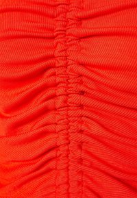Tessuto rosso brillante con un design texturizzato e arricciato. Il materiale sembra elastico, mostrando una serie di arricciature parallele sulla superficie.
