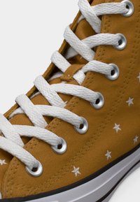 Κίτρινο ανδρικό ψηλό αθλητικό παπούτσι με μοτίβα λευκών αστεριών, λευκά κορδόνια, ασημί οπές και μαύρη λαστιχένια σόλα με ρίγες.