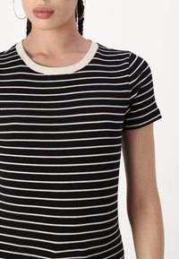 T-shirt à manches courtes rayé noir et blanc avec une texture côtelée et un col arrondi de couleur crème contrastant.