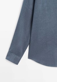 Blauwgrijs shirt met lange mouwen, manchetten aan de polsen en een afgeronde zoom, afgebeeld tegen een witte achtergrond.