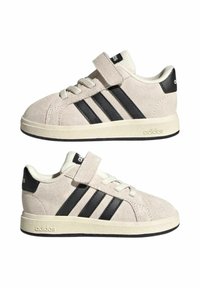 Adidas sneakers in light beige suede with black three stripes and black heel tab. Features lace and Velcro closure, textured rubber sole.