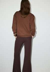 Sudadera de punto marrón de manga larga, combinada con pantalones de campana marrones de cintura alta, que presentan una textura suave y un diseño ajustado.