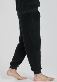 Schwarze Fleece-Jogginghosen mit weicher, strukturierter Oberfläche; enganliegende Bündchen und elastischer Taillenbund. Seitentaschen sichtbar auf der Vorderseite.