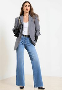 Pelēks žakets ar sarullētām piedurknēm, balta blūze, gaiši zili platajās bikses, un melnas cimdi. Melna rokassoma un norādīti papēži papildina komplektu.