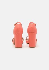 Coral high-heeled sandals with a smooth leather finish, showcasing a wide block heel and ankle strap with a round buckle detail.