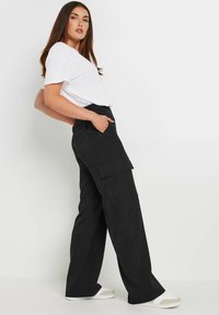 Zwarte cargobroek met een losse pasvorm, voorzien van meerdere grote zakken. Gecombineerd met een eenvoudig wit T-shirt en casual witte sneakers.