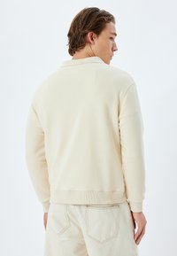 Crème-kleurige sweatshirt met een relaxte pasvorm, voorzien van een geribde halslijn en manchetten, gemaakt van zachte stof, gecombineerd met lichtbeige broek.