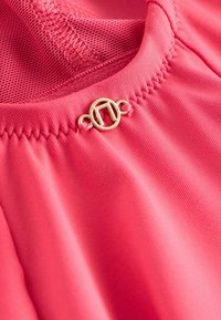 Rožinės spalvos sportinė palaidinė su tinklelio panelėmis, siuvinėjimo detalėmis ir aukso spalvos apvalia metaline sagtele. Lyčio tekstūra ir lengva medžiaga.